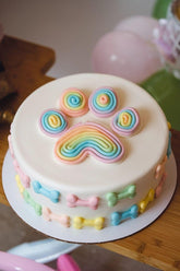 Colorful rainbow paw print cake with pastel bone decorations, perfect for pet celebrations.