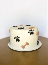 TPS Signature Paw Cake featuring black and tan paw and bone decorations on a minimalist white cake.