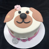 Cute pink pup celebration cake featuring dog face design and flower decoration, perfect for pet birthdays.